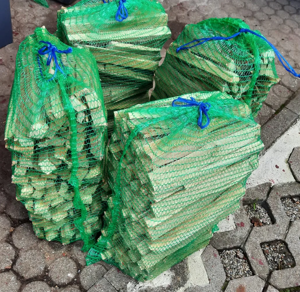Vier grüne Netzsäcke mit fein gespaltenem Anzündholz auf dem gepflasterten Hof