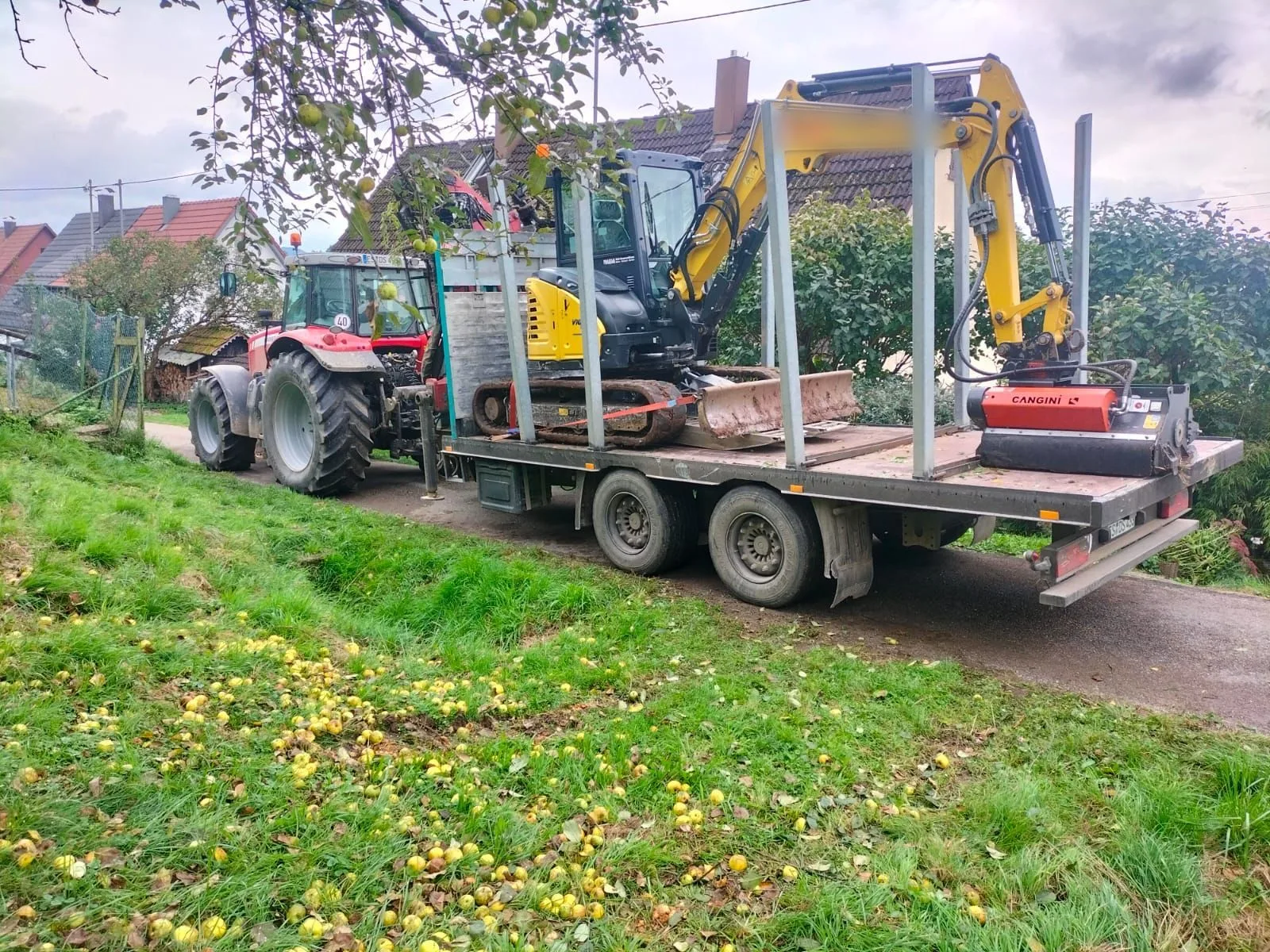 Minibagger mit Mulchkopf verzurrt auf dem Tieflader hinter dem Schlepper auf dem Weg zum Einsatzort
