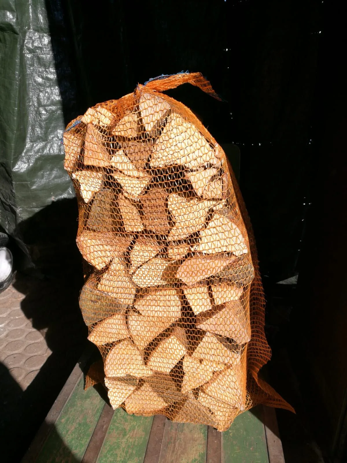 Praller orangener Netzsack mit ofenfertigem Scheitholz auf einer Holzpalette