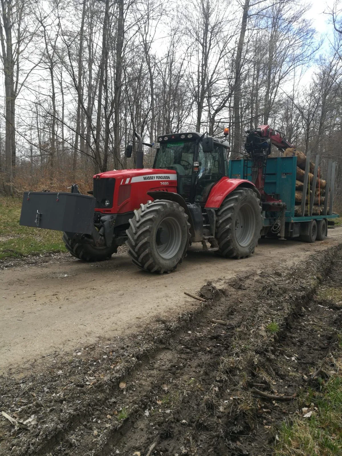 Massey Ferguson mit beladenem Rückewagen auf dem Waldweg im kahlen Winterwald