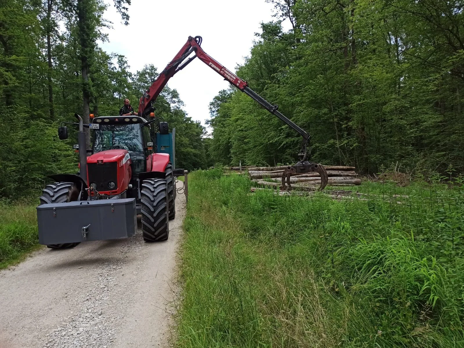 Schlepper mit Rückewagen auf dem Waldweg, der Kran greift nach dem Langholz am Wegrand